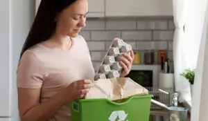 woman-recycling-cardboard-egg-carton-green-bin-kitchen